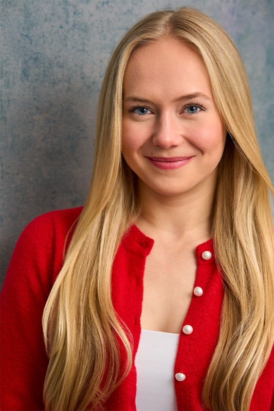 Actor headshot in a red cardigan against a grey backdrop